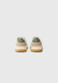 Tenisi cu o parte superioară din suede bej și verde, talpă intermediară crem și talpă din cauciuc, având un design simplu și accente de culoare minime.