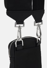 Borsa nera in tessuto con zip e accessori in argento. Presenta una tracolla regolabile con ganci a scatto e una finitura testurizzata. Design compatto.