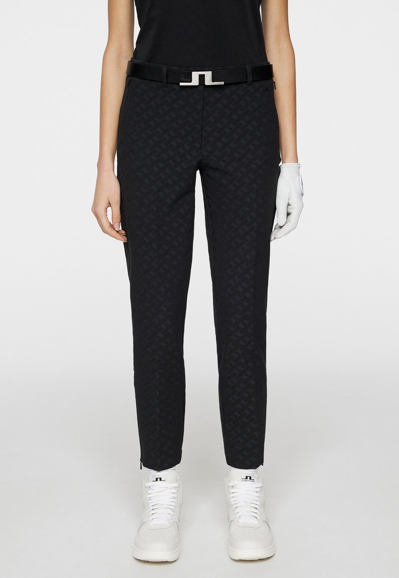 Svarta mönstrade byxor med slim fit, som har ett glänsande svart bälte med en silverklämma. Bärs med vita sneakers och en svart topp.