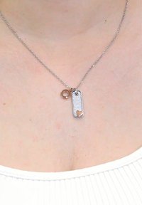 Collana in argento con un pendente a tag dog texturizzato con un'intaglio a forma di cuore e un piccolo charm circolare.