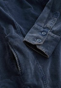 Granatowa koszula z korduroy z kołnierzykiem, dwoma guzikami przy mankietach oraz subtelnym, pionowym prążkowaniem.