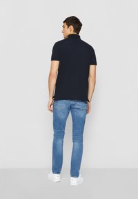 Navy-Polo-Shirt mit kurzen Ärmeln und Kragen, kombiniert mit hellblauen Slim-Fit-Jeans und weißen Sneakern. Einfaches, lässiges Design.