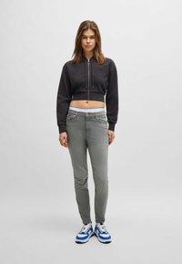 Musta lyhyt huppari, jossa on edessä vetoketju, yhdistettynä vaaleanharmaisiin slim-fit-farkkuihin. Varustettu valkoisilla ja sinisillä yksityiskohdilla varustetuilla lenkkareilla. Yksinkertainen muotoilu.