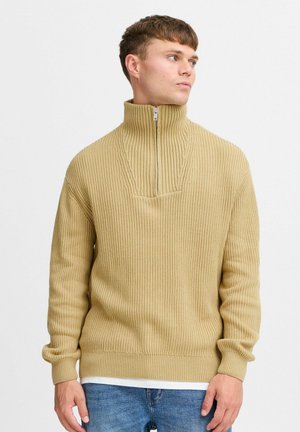 Beige ribbed pullover sweater with a high collar, half-zip front, long sleeves, and a relaxed fit. Textured knit fabric.