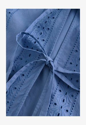 Vaaleansininen kangas, jossa on brodeeratut kukkakuviot, leikkaukset ja vyötäröllä sidottu yksityiskohta. Pehmeä tekstuuri, rento muotoilu.