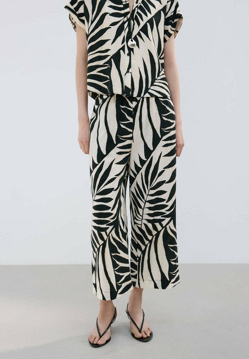 Femme portant un pantalon court ample noir et blanc à motif feuilles et un haut à manches courtes assorti avec des sandales noires à brides.