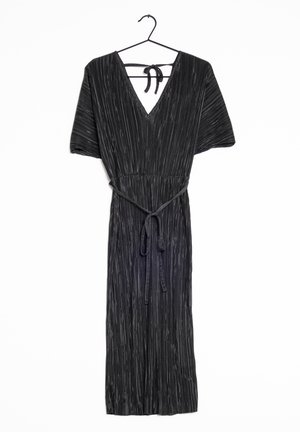 Robe midi plissée noire avec manches courtes, col en V, ceinture à nouer à la taille et lien à nouer au cou à l'arrière, suspendue sur un cintre contre un fond blanc.