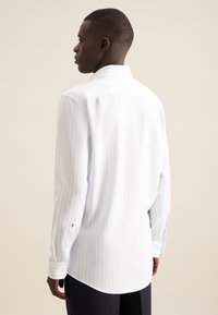 Camicia bianca a maniche lunghe con righe azzurre chiare, con colletto classico e polsini con bottoni. Tessuto elegante e testurizzato con una finitura liscia.