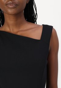 Robe noire à une épaule avec un col structuré, présentant une texture lisse et des lignes épurées. Sans manches avec un corsage ajusté.