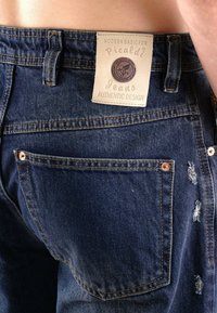 Denimjeans mit einer hellen Wäsche, sichtbarem Gebrauch, einem Markenetikett am Bund, Kupferbeschlägen und Stichdetails an den Gesäßtaschen.