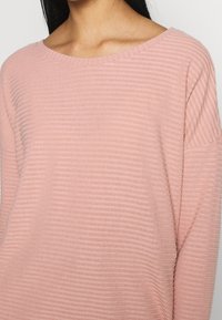Helle rosa Pullover mit gerippter Textur, weitem Ausschnitt und überschnittenen Ärmeln, aus weichem Material für eine lockere Passform.