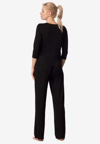 Czarny zestaw dresowy składający się z bluzki z rękawami o długości trzech ćwiartek z falbaniastym dekoltem oraz luźnych spodni o prostym kroju wykonanych z miękkiego materiału.