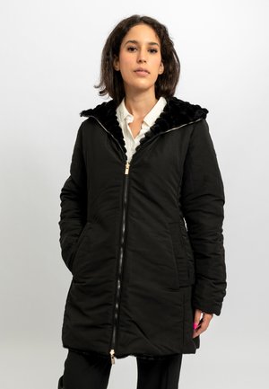 Cappotto imbottito nero con cappuccio di pelliccia, chiusura con zip, tasche laterali e texture morbida. Presenta una zip dorata e un design fino al ginocchio.