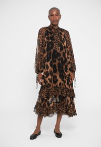 Abito midi con stampa leopardata, maniche lunghe, collo con fiocco e orlo a strati in tessuto trasparente. Colori marrone e nero con un tessuto fluido e leggero.
