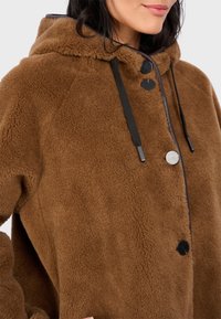 Brauner Fleece-Hoodie mit weichem Material, ausgestattet mit schwarzen Knöpfen und Kordelzügen. Kapuzen-design mit lockerer Passform.