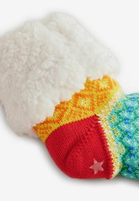 Bunte gestrickte Socke mit einem flauschigen weißen Bund, verziert mit roten, gelben und grünen Mustern sowie einem kleinen roten Sternakzent an der Zehe.