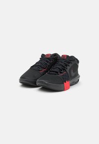 Baskets de sport noires avec un dessus en maille texturée, accents rouges au niveau du talon et des lacets, dotées d'une semelle rembourrée et d'un logo distinct sur la languette.