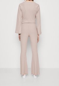 Beige ribbad tvådelad outfit med en långärmad topp och svängda byxor, som visar en mjuk textur och en enkel design.