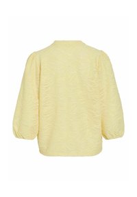 Blouse jaune clair texturée avec manches longues bouffantes et poignets élastiques, vue de dos sur un fond blanc.