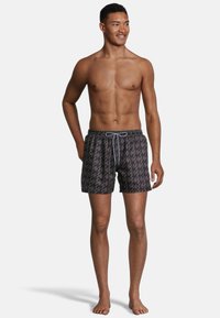 Swim shorts in dark gray with a geometric pattern, elastic waistband, and drawstring. Mid-thigh length with a smooth fabric texture.