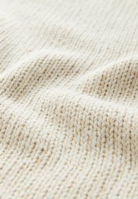 Gros plan sur un tissu tricoté doux de couleur crème, montrant une texture côtelée détaillée et des ombres subtiles à la surface.