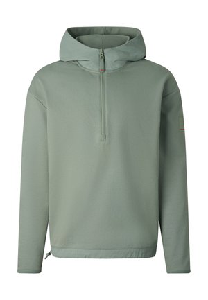 Man staat en draagt een saliegroene hoodie met ritssluiting aan de voorkant, bijpassende korte broek, witte enkelsokken, grijze sneakers en reflecterende oversized zonnebril.