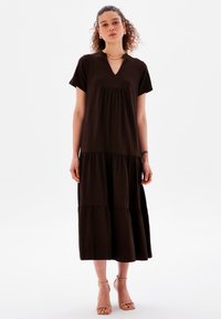 Braunes knielanges Kleid mit V-Ausschnitt, kurzen Ärmeln und gestuftem Design. Hergestellt aus weichem Stoff mit glatter Textur.