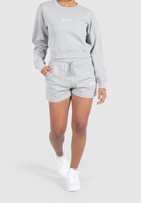 Felpa grigia chiara con design cropped e maniche lunghe, abbinata a pantaloni shorts grigi coordinati con vita elastica e tasche.
