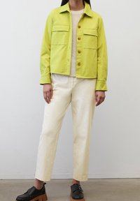 Jasnozielona krótka kurtka z dwoma przednimi kieszeniami, zapinana na guziki, w połączeniu z kremowymi, luźnymi spodniami i czarnymi butami na platformie.