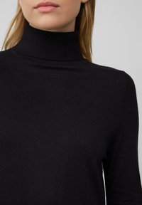Schwarzer Rollkragenpullover mit tailliertem Design, geripptem Kragen und weicher Textur. Hat lange Ärmel und dezente Nähdetails.