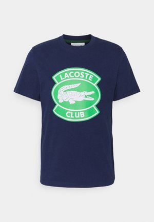 Granatowy T-shirt z krótkim rękawem z zielonym i białym logo Lacoste Club, na środku którego znajduje się krokodyl.