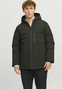 Chaqueta acolchada de color verde oscuro con capucha, que cuenta con un cierre frontal y un bolsillo en el pecho, fabricada con un material suave y resistente al agua.
