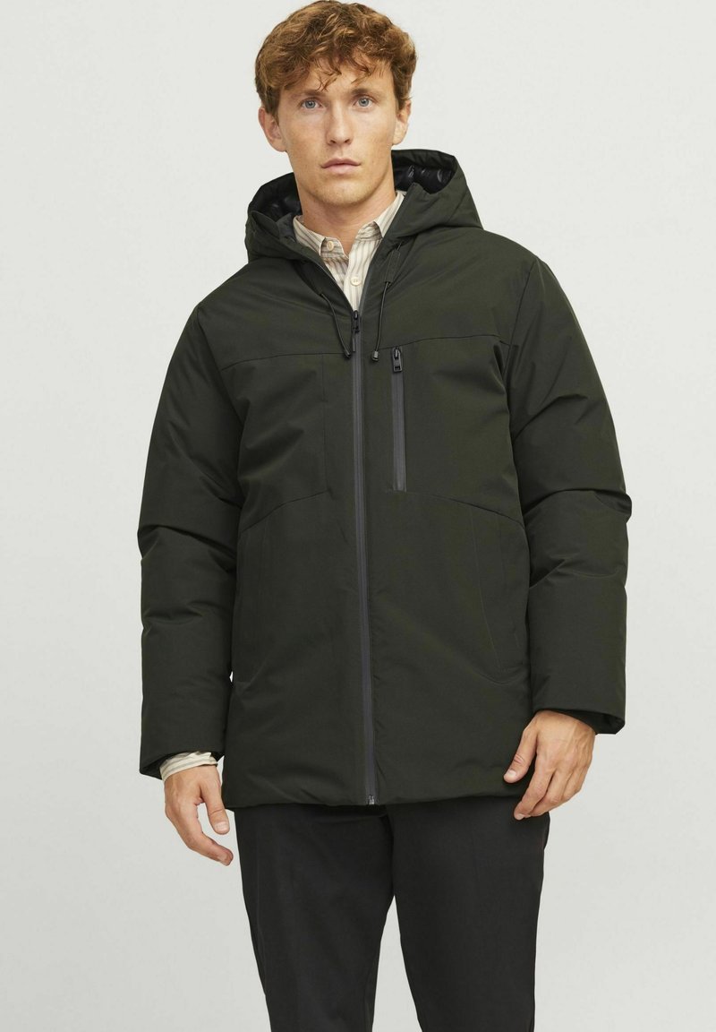Chaqueta acolchada de color verde oscuro con capucha, que cuenta con un cierre frontal y un bolsillo en el pecho, fabricada con un material suave y resistente al agua.