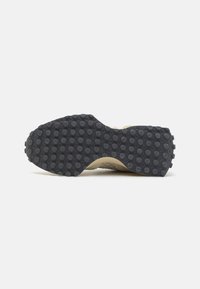 Black rubber outsole with textured, circular tread pattern; beige upper with woven texture; sturdy construction.