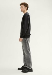 Czarna bluza z okrągłym dekoltem, w połączeniu z szarymi, luźno dopasowanymi dżinsami oraz czarnymi butami, prezentując prosty i casualowy styl.