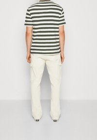 Camiseta de manga corta a rayas verdes y blancas con cuello redondo, combinada con pantalones cargo crema que cuentan con bolsillos laterales y un corte relajado.