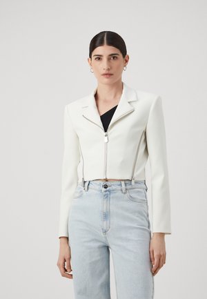 Giacca corta in ecopelle bianca con zip frontale, colletto sagomato e accessori in argento, abbinata a jeans azzurri a vita alta.