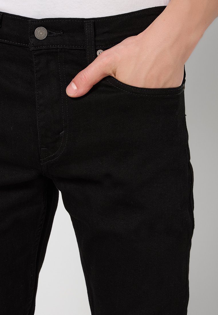 Schwarze Denim-Jeans mit klassischem Fünf-Taschen-Design. Der Stoff hat eine subtile Textur, und ein Metallknopf am Bund ist sichtbar.