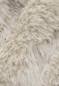 Gros plan sur un tissu tricoté beige doux avec une texture duveteuse, floue et un motif tissé visible.
