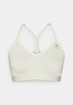 Light beige sports bra with a V-neck design. Features thin, crisscross straps and a smooth texture. Logo printed on the left side.
