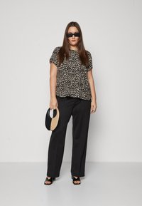 Leopardprint T-shirt met korte mouwen, zwarte hoge taillebroek, zwarte sandalen met blokhak en open teen, en een twee-kleurige handtas die in één hand wordt vastgehouden.