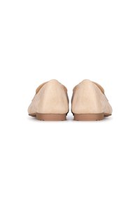 Zapatos sin cordones de ante beige con suela plana marrón, punta redondeada y un detalle de costura minimalista en la parte trasera. Textura suave.