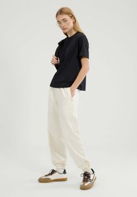 Marineblaues T-Shirt mit kurzen Ärmeln und lockerer Passform, kombiniert mit cremefarbenen Jogginghosen mit Reißverschlusstaschen und braunen und weißen Sneakers.