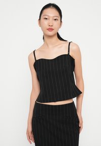 Top corto negro con escote en forma de corazón, finas tirantes ajustables y rayas blancas verticales. Presenta dos bolsillos frontales.