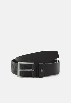 Ceinture en cuir noir roulée avec boucle rectangulaire argentée et logo subtilement embossé sur la sangle près de la boucle.