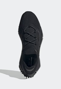 Svart träningsskor med överdel i stickat material, texturerad yta och gummisula. Har integrerade snörningar och en minimalistisk design.