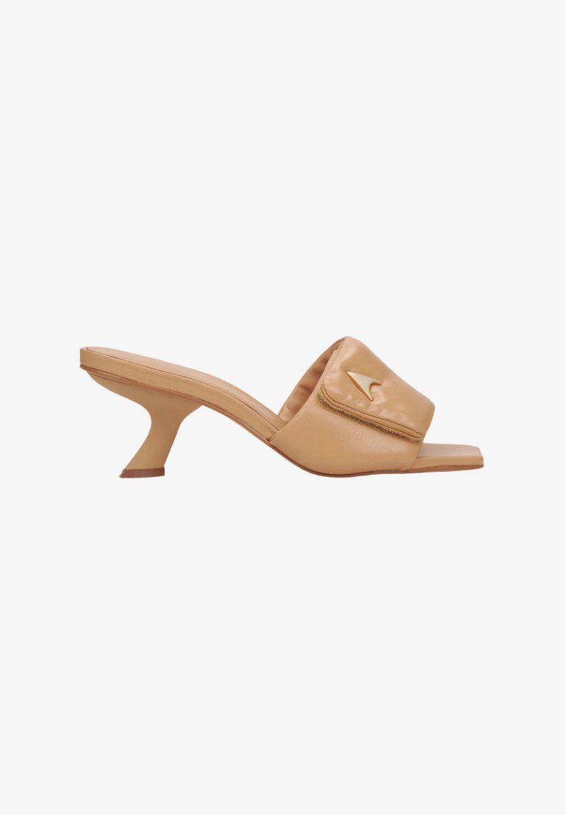 Beige leather open-toe mules with a padded upper, curved heel, and a small embossed logo detail on the front. Smooth texture.