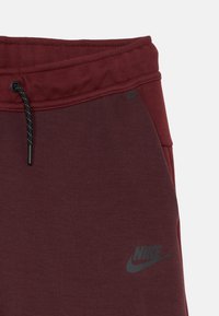 Bordo spalvos treningai su elastingu juosmeniu, su raišteliu ir pilku Nike logotipu. Medžiaga lygi ir šiek tiek tekstūruota.