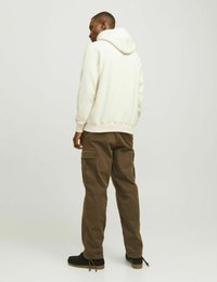 Bílá mikina s kapucí a olivově zelené cargo kalhoty s bočními kapsami, nošené s černými botami s texturovanou podrážkou.