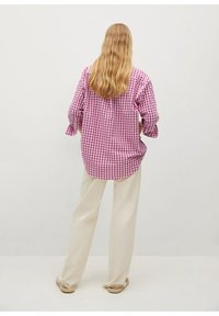 Camisa de cuadros en rosa y blanco con mangas largas y dobladillo curvado, combinada con pantalones de pierna ancha en color crema y zapatos de lona beige.
